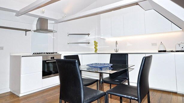 A modern kitchen with white cabinetry, a gas stove, and a glass dining table with black chairs. - Newly Refurbished 1 Bedroom Whitechapel (London)