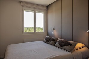 Une chambre à coucher avec un lit, deux oreillers, une fenêtre et une lampe fixée au mur.