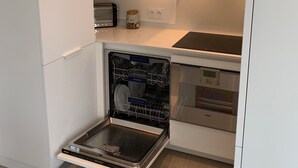 A compact kitchen with white cabinetry, a built-in dishwasher, a toaster, and a small countertop with a jar. - Superb view of the ocean, the beach at your feet! (Soorts-Hossegor)