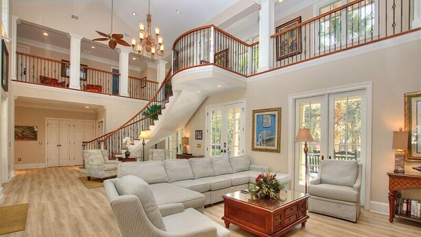 A spacious living room with a large sectional sofa, a coffee table, and a staircase leading to an upper level. - 48 S. Sea Pines Dr - Luxury Home in Sea Pines w/ Game Rm, Media Rm, Private Pool (Hilton Head Island)