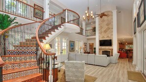 A spacious living area with a curved staircase, a fireplace, and a large TV. - 48 S. Sea Pines Dr - Luxury Home in Sea Pines w/ Game Rm, Media Rm, Private Pool (Hilton Head Island)