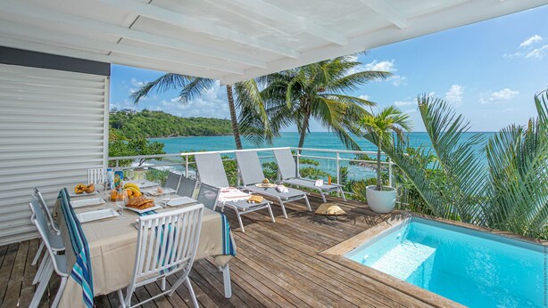 A covered outdoor area with a pool, lounge chairs, and a table set for dining. - Villa Leynita Bay, 5 bedrooms, sleeps 12 on the beach of Diamant Martinique  (le diamant)