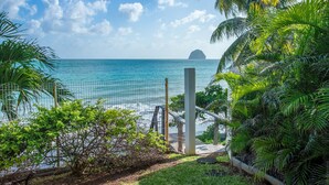 A tropical beach view with a clear sky, palm trees, and a fence overlooking the ocean. - Villa Leynita Bay, 5 bedrooms, sleeps 12 on the beach of Diamant Martinique  (le diamant)