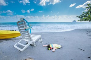 Una silla de playa con un chaleco salvavidas, una tabla de surf amarilla y una tabla de remo sobre la arena.