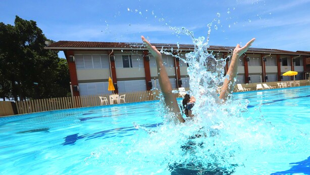 Une piscine dans laquelle une personne plonge, entourée de chaises longues et d’un bâtiment doté d’un toit en tuiles.