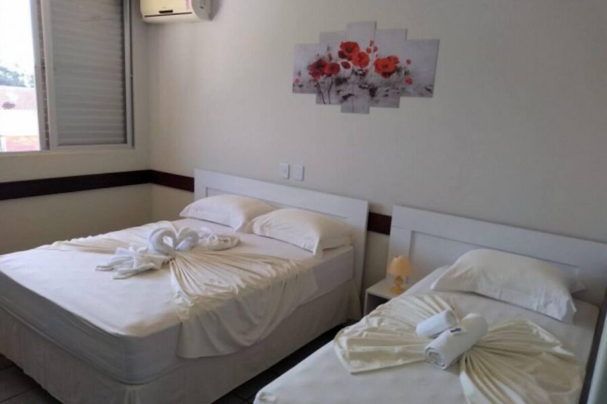 Quarto de hotel com duas camas, cada uma com toalhas dobradas e cabeceira branca.