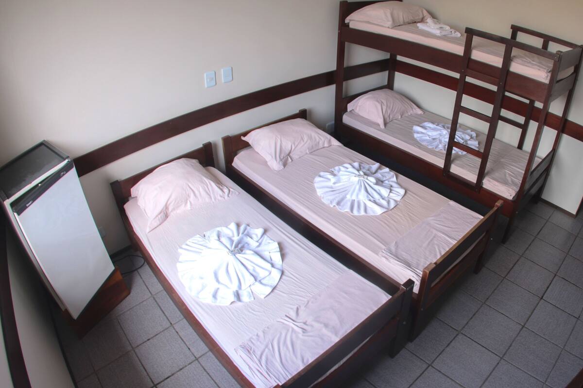 Um quarto de dormitório com beliches, uma escrivaninha e um pequeno frigorífico.