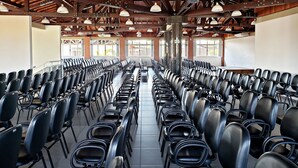 Une salle de conférence avec des rangées de chaises noires, des poutres en bois au plafond et de grandes fenêtres.