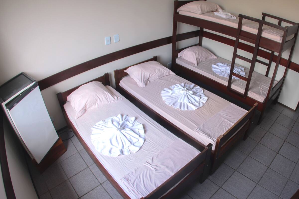 Quarto de dormitório com três beliches, uma escrivaninha pequena e uma cadeira.