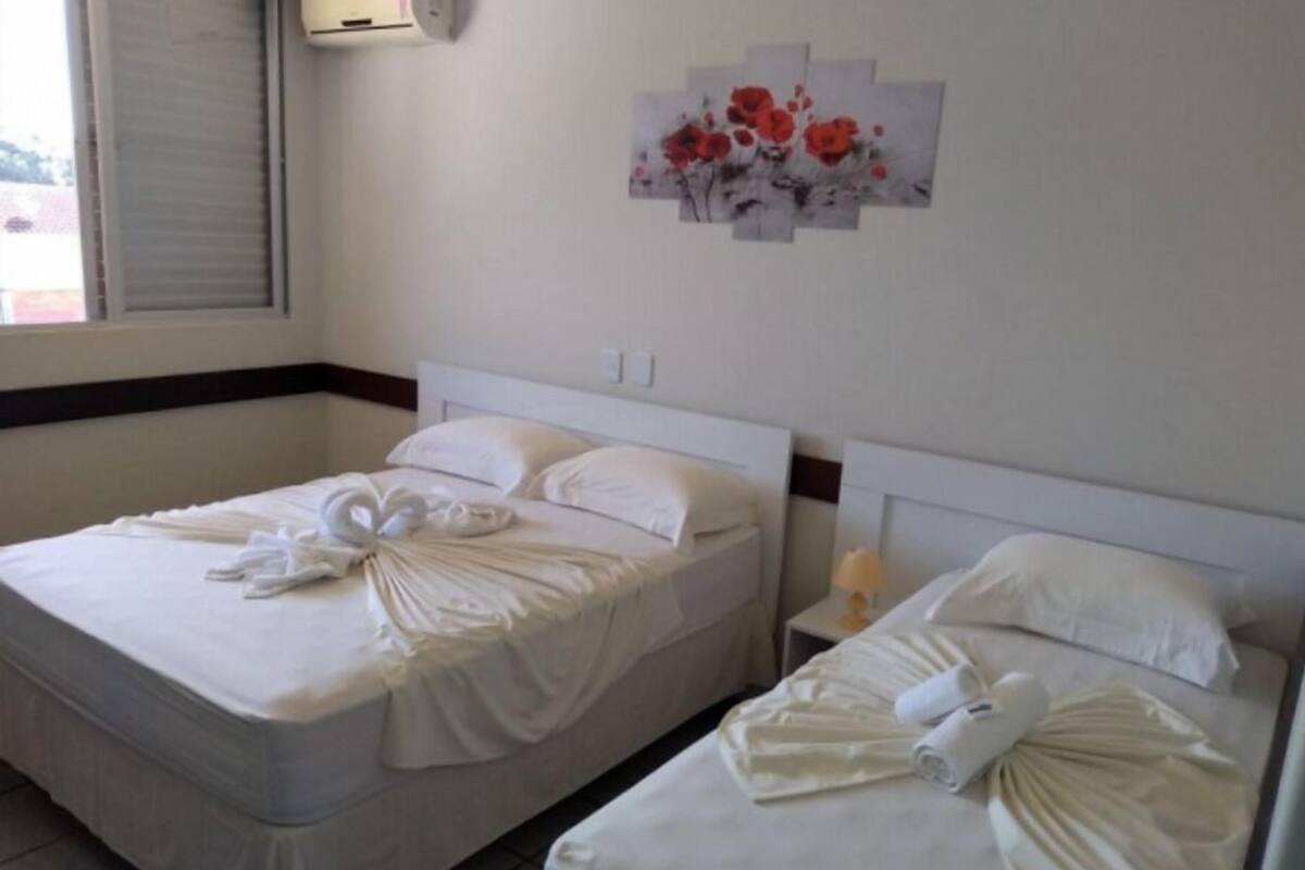 Quarto de hotel com duas camas, cada uma com toalhas dobradas e cabeceira branca.