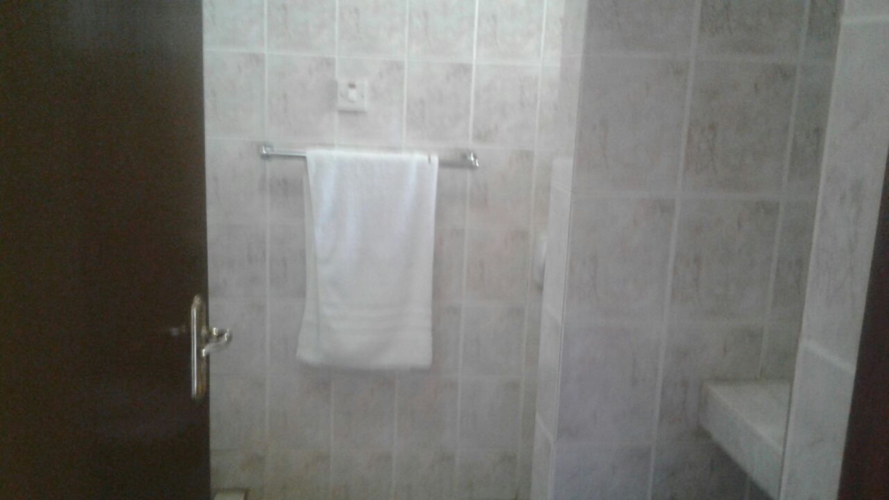 A bathroom with a tiled wall, a towel hanging on a rack, and a door.