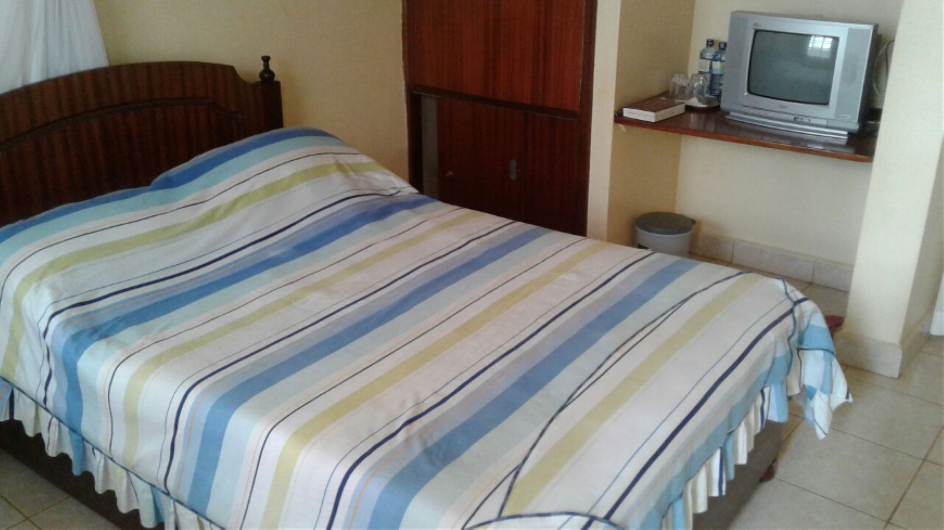 Un dormitorio con cama, armario de madera, televisor en un estante y un cesto de basura.