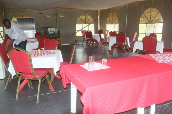 A tented dining area with tables and chairs, a television, and a person arranging the tables.