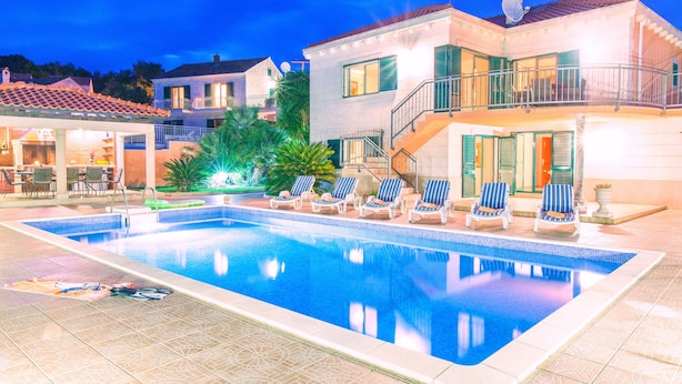 A swimming pool with lounge chairs, a covered patio, and a staircase leading to a balcony.
