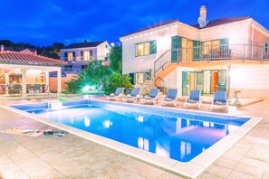 A swimming pool with lounge chairs, a covered patio, and a staircase leading to a balcony.