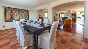 A dining area with a dark wooden table, white upholstered chairs, and a large painting on the wall.