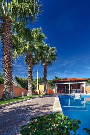 A pool area with palm trees and a building with a red roof.