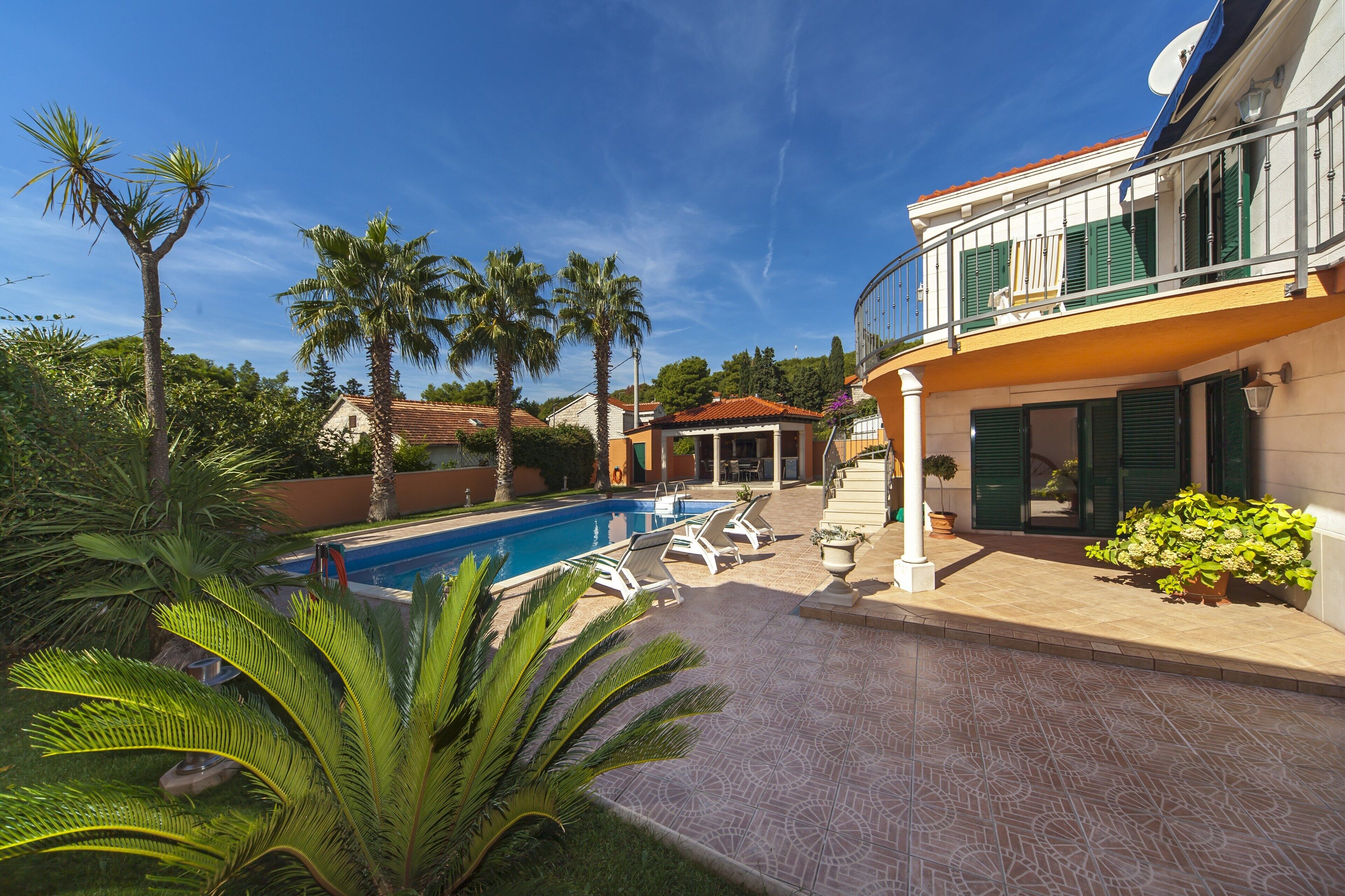 A swimming pool with lounge chairs, palm trees, and a building with a balcony.