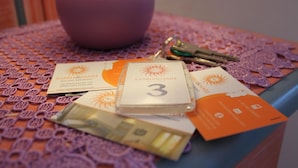 Una mesa con un florero morado, llaves, tarjetas de presentación y un cuadernillo.