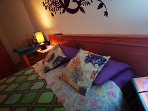 A bedroom with a bed, pillows, a nightstand, a lamp, and a wall decoration. - Sabbia e Mare (Porto Torres)