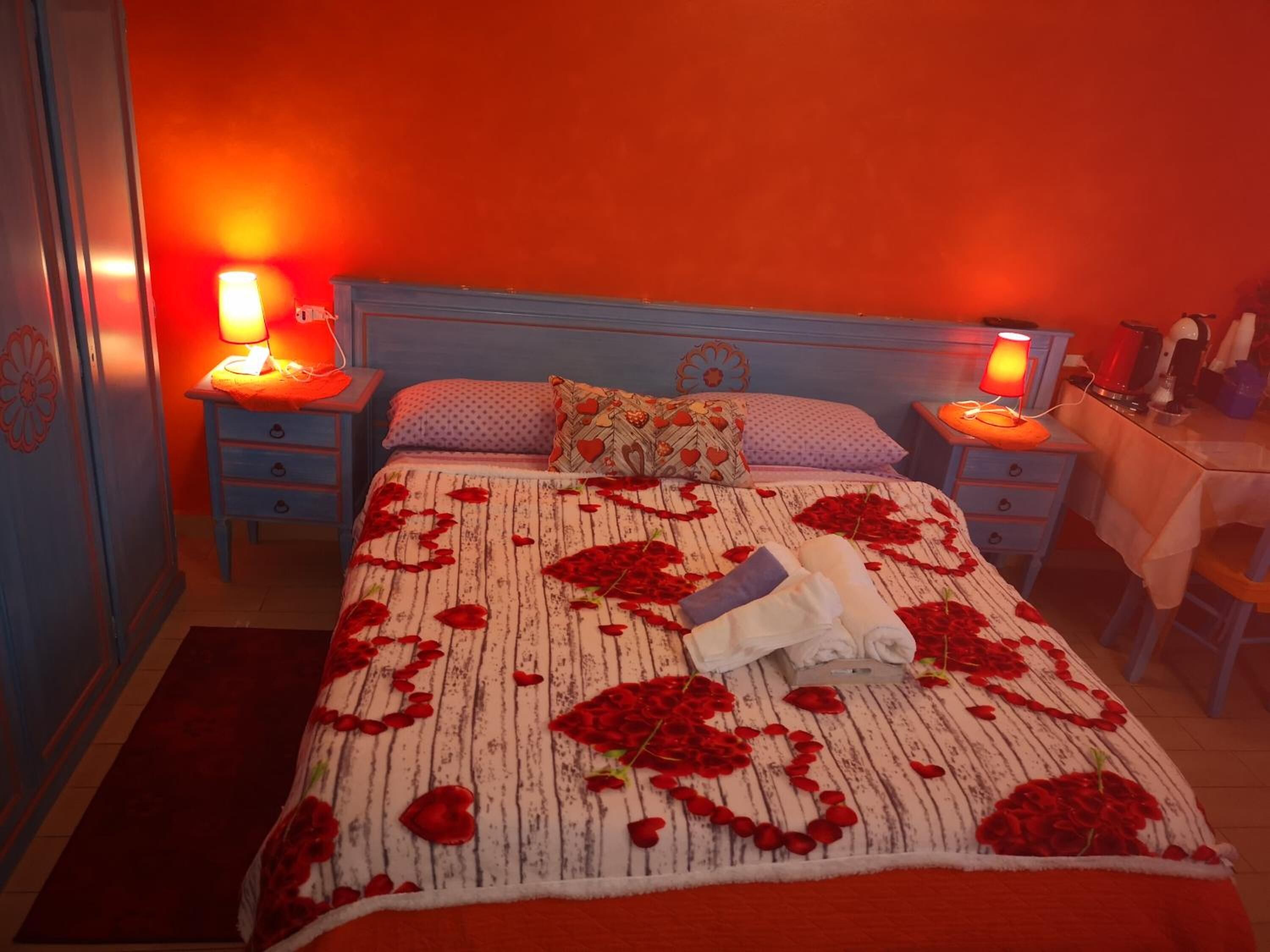 A bedroom with a bed adorned with rose petals, two bedside lamps, and a nightstand with a lamp.