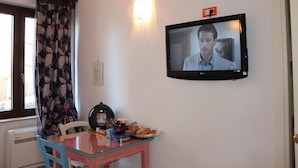 Una habitación con una mesa de comedor, sillas, un televisor montado en la pared, una ventana con cortinas y un radiador.