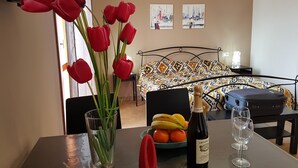 A room with a bed, a table with a bottle of wine, glasses, and a vase with red flowers. - POMPEI - LARA SUITE (Scafati)