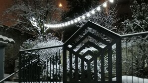 Un espacio exterior cubierto de nieve con una valla metálica, una construcción pequeña y luces colgantes.
