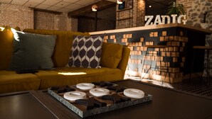 Un interior moderno con un sofá amarillo, almohadones estampados, una mesa de centro con objetos geométricos y una pared de ladrillo con letreros 'ZADIG'.