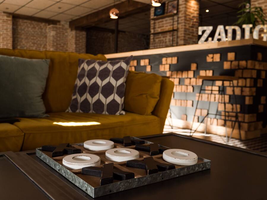 A modern interior with a yellow sofa, patterned pillows, a coffee table with geometric objects, and a brick wall with 'ZADIG' signage.