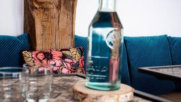 A wooden table with a bottle of water, glasses, and a floral pillow on a blue sofa.