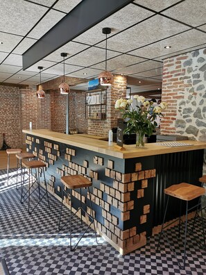 A bar area with a checkered floor, a brick wall, and a wooden counter. - Hotel Zadig (Aurillac)