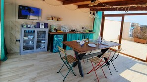 A wooden ceiling with string lights, a dining table with chairs, a refrigerator, and a television on the wall.