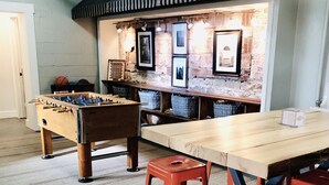 Quarto com mesa de pebolim, mesa de madeira comprida e banquetas vermelhas.