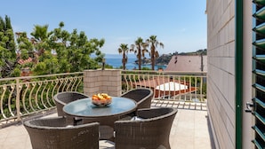 Een balkon met rieten meubels, een tafel met een schaal fruit en uitzicht op zee en palmbomen.