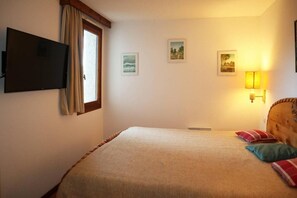 Ein Schlafzimmer mit einem Bett, einem an der Wand befestigten Fernseher und einem Fenster mit Vorhängen.