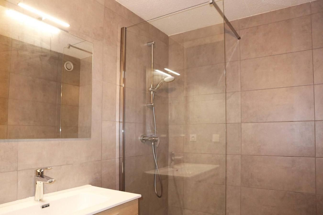 Ein modernes Badezimmer mit einer gläsernen Dusche, einem weißen Waschbecken und einem Spiegel.