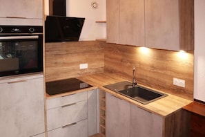 A compact kitchen with a built-in oven, a sink, and wooden cabinetry.