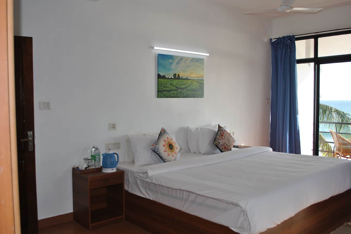 A bedroom with a bed, a nightstand, a painting, and a view of the ocean.