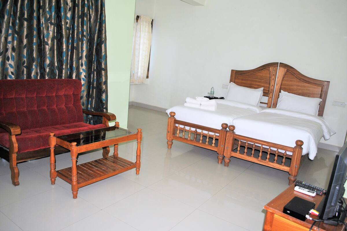 A hotel room with a wooden bed, a red sofa, a wooden coffee table, and a television on a wooden stand.