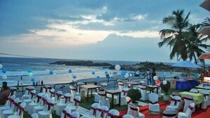 Een evenementenopstelling buiten, met witte stoelen en tafels, een rode loper en uitzicht op de oceaan.