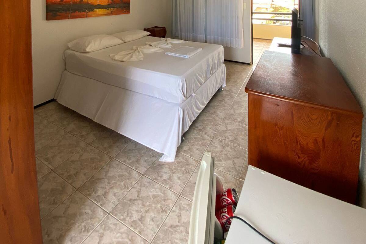 A bedroom with a bed, a wooden desk, a painting, and a view through a window with curtains.