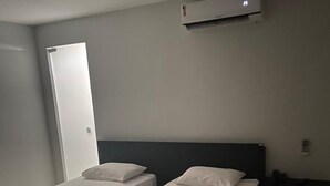 A hotel room with two single beds, a bedside table with a towel, a wall-mounted air conditioner, and a door.