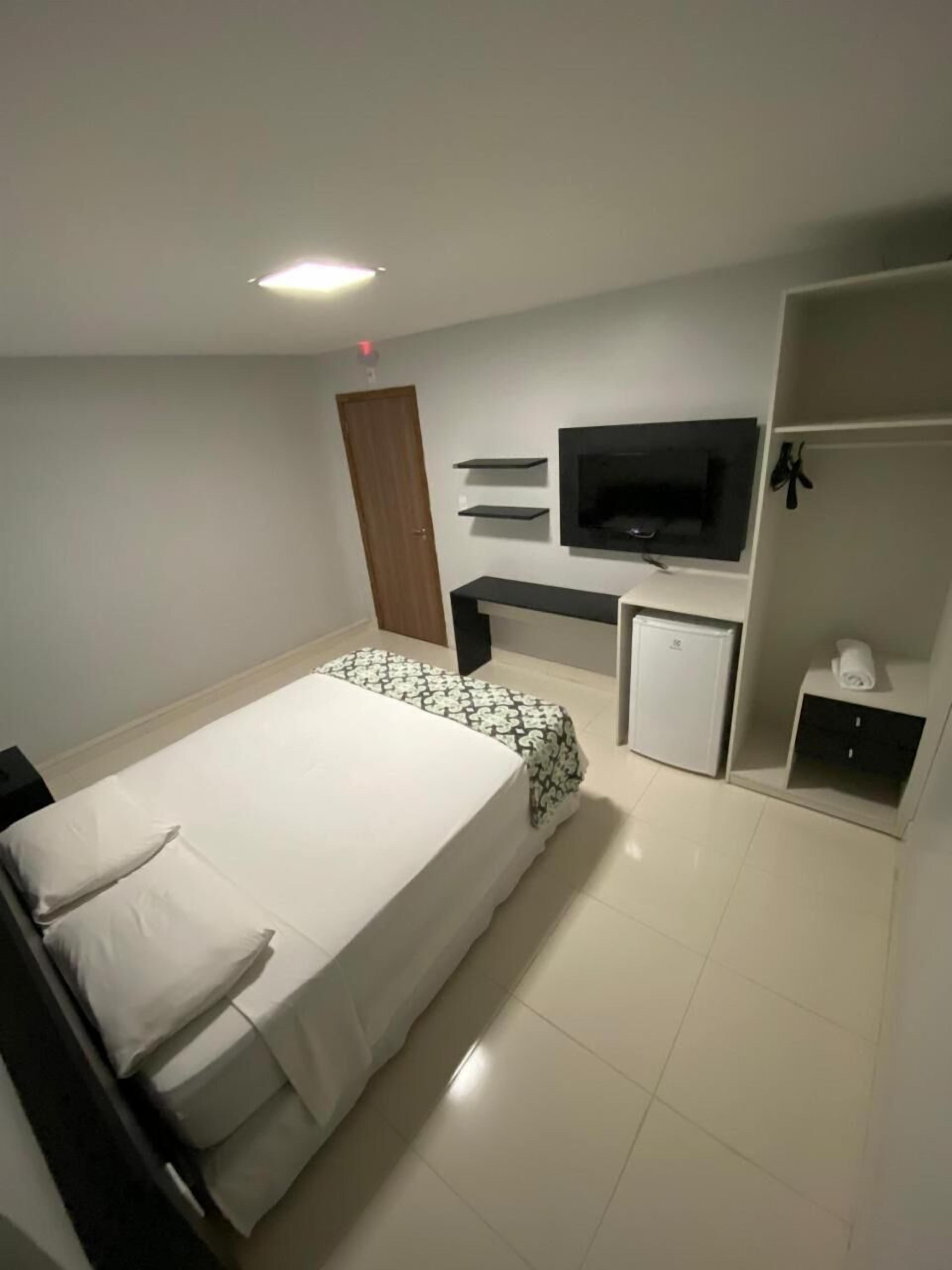 A modern hotel room with a large bed, a TV mounted on the wall, a small desk, and a wardrobe.