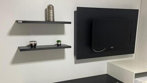 A modern, minimalist room with a black desk, a grey chair, and a mounted TV on the wall.