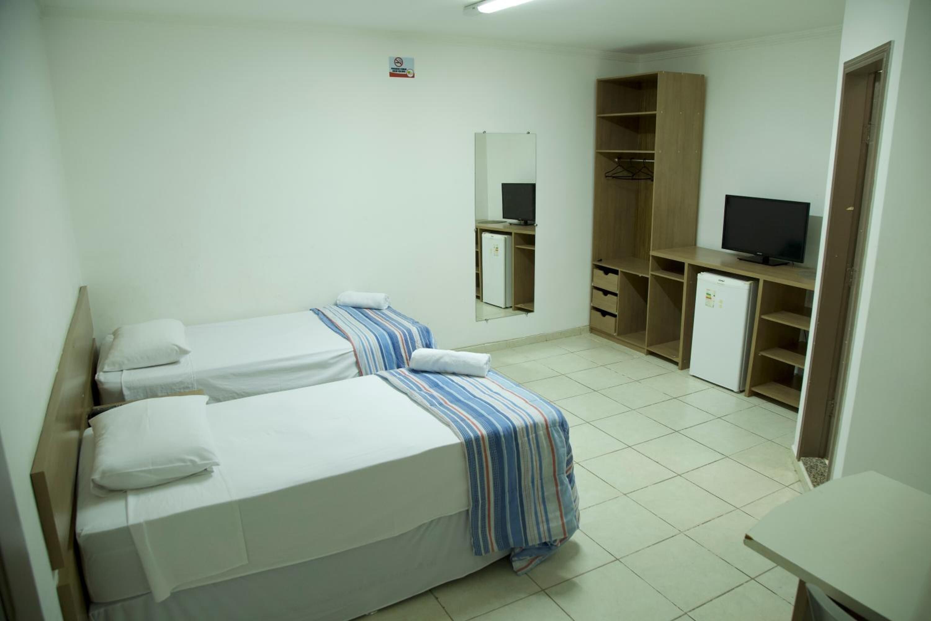 Une chambre d’hôtel avec deux lits, une télévision, un miroir et une armoire.