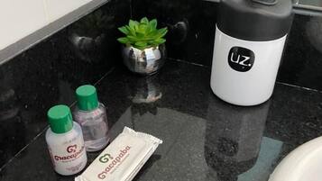 Un baño con encimera negra, una pequeña planta en maceta, una botella de Gracapab, un paquete de Gracapab y una botella de agua blanco y negro con el logo 'UZ'.
