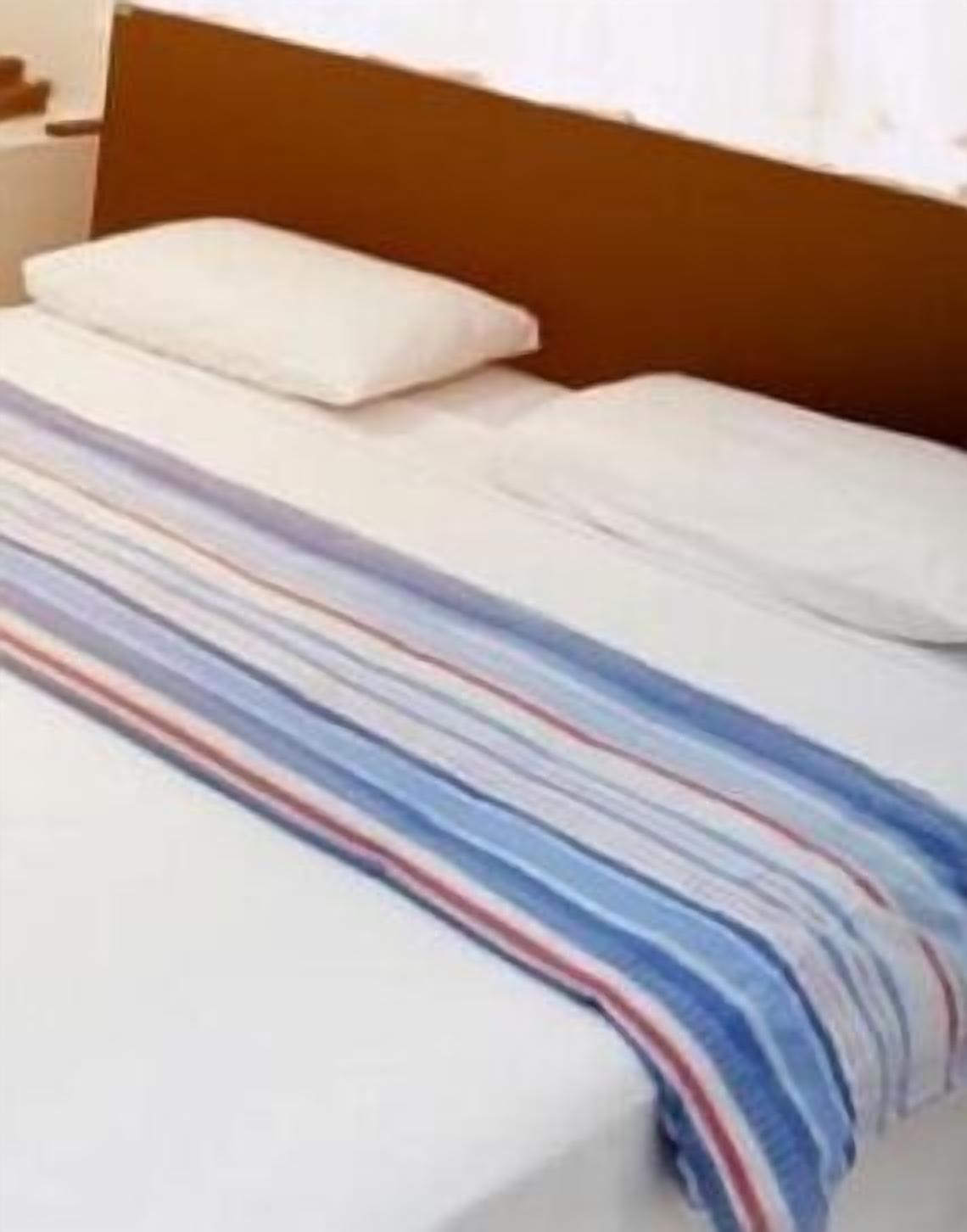 Un lit avec une couverture à rayures, une tête de lit en bois et des oreillers blancs.