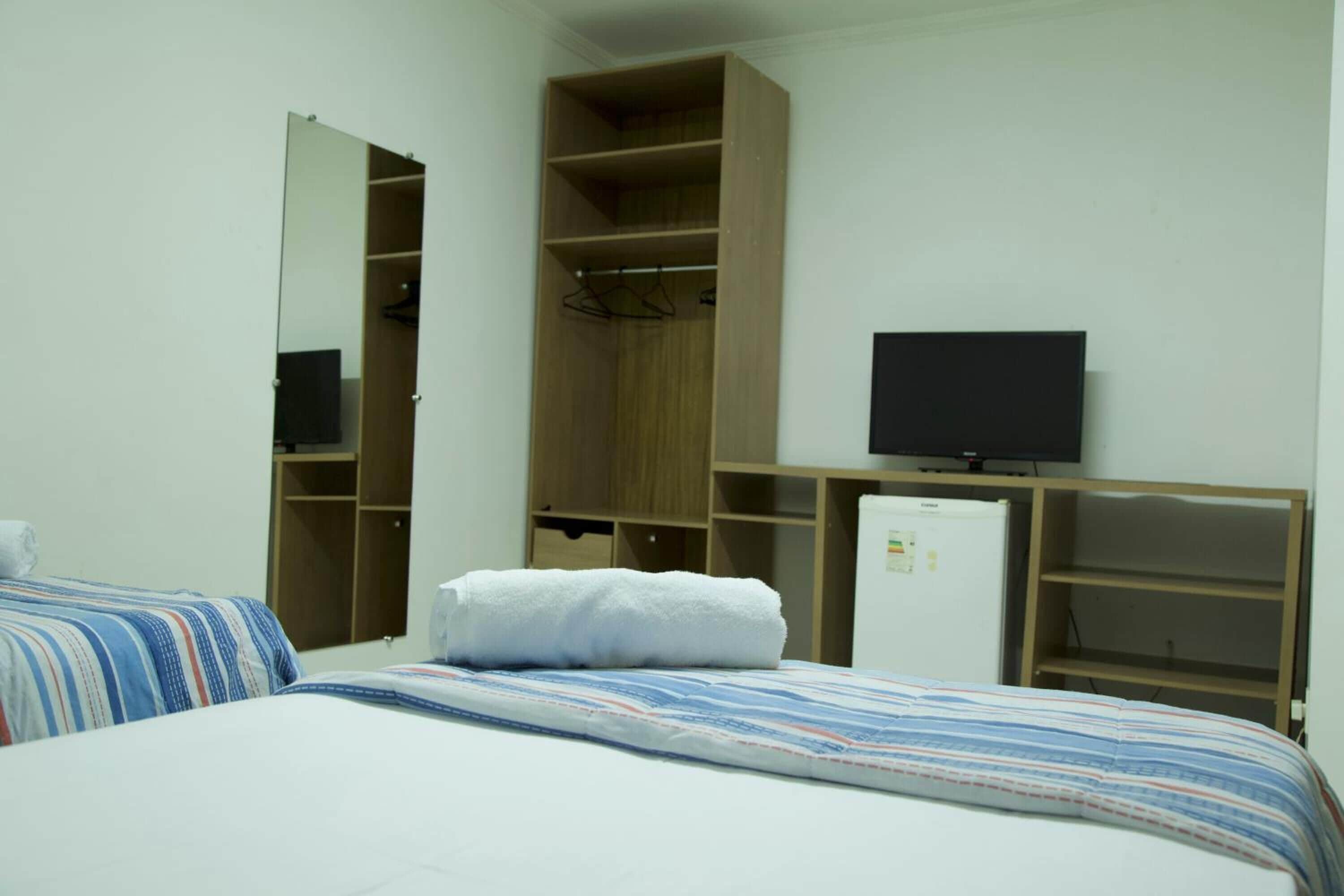 Un dormitorio con cama, armario, televisor y refrigerador.