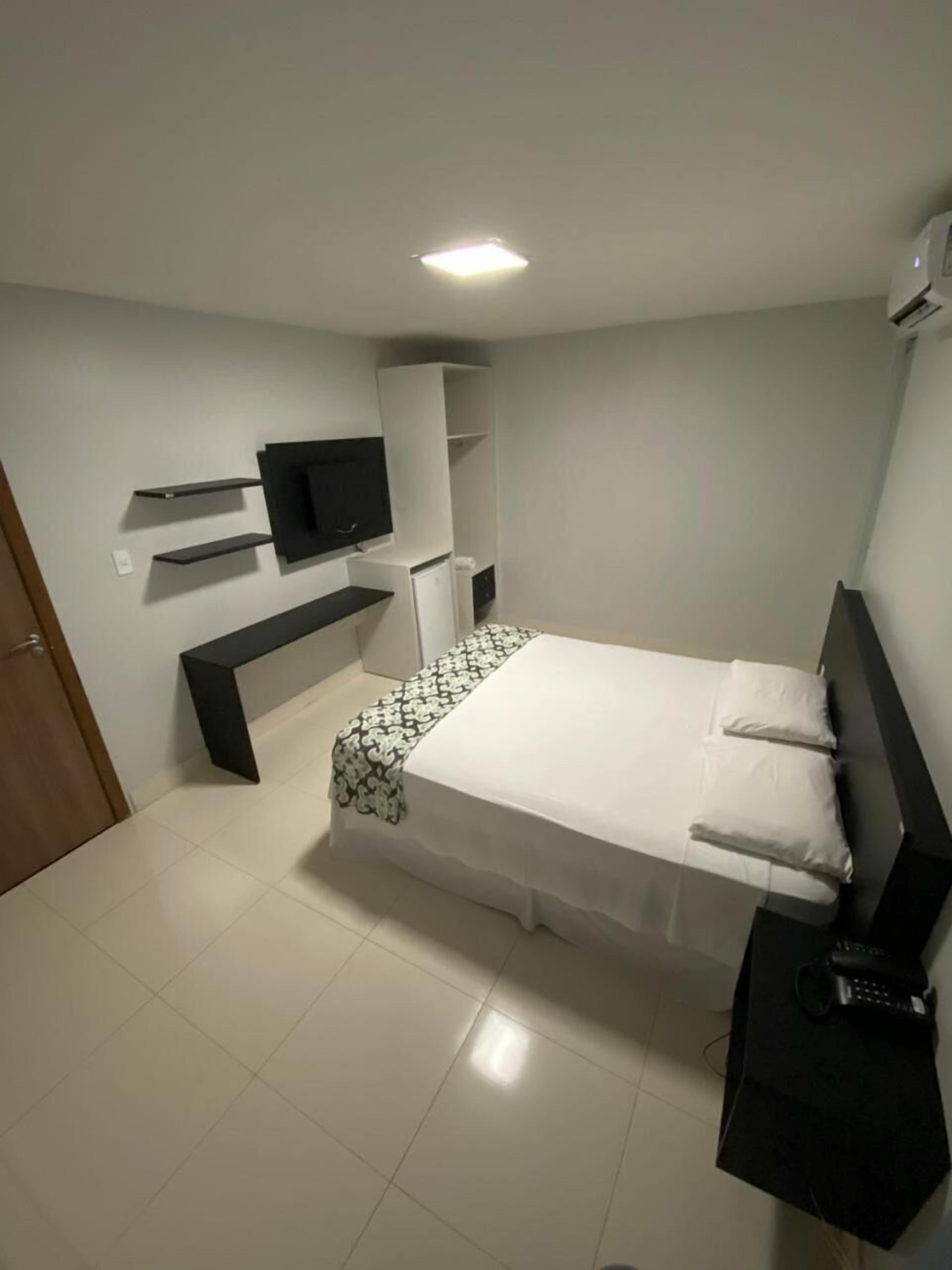 A bedroom with a bed, a TV mounted on the wall, a small desk, and a wardrobe.